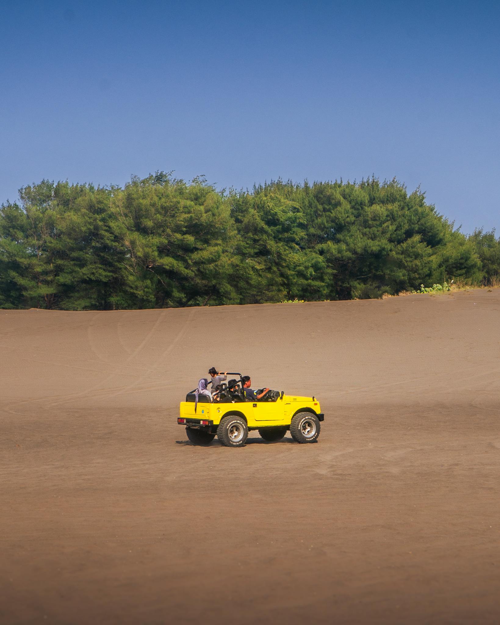 Yellow jeep driving through desert landscape under clear blue sky.