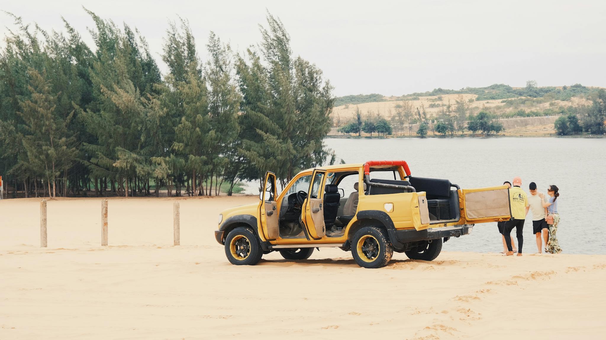 Yellow off-road jeep on sandy lakeside with people exploring the natural scenery.
